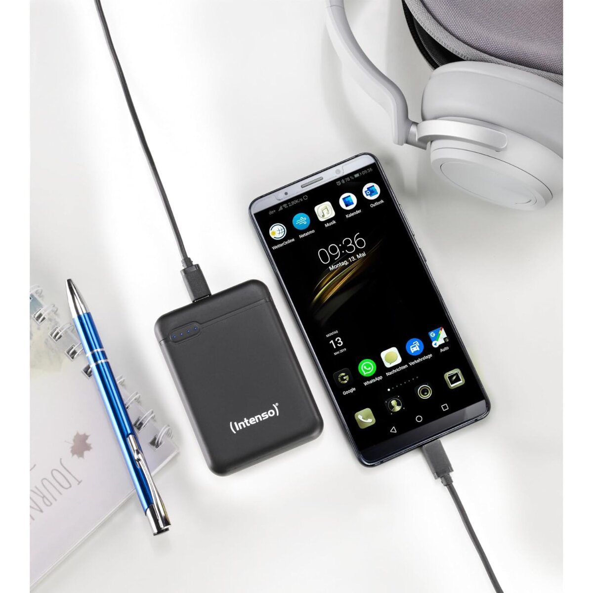 Zwarte powerbank laadt smartphone op, met pen en koptelefoon ernaast.