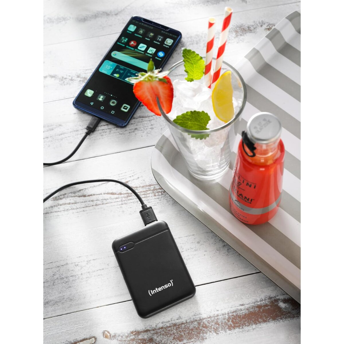 Zwarte smartphone wordt opgeladen door een powerbank, ernaast een glas met drankje.