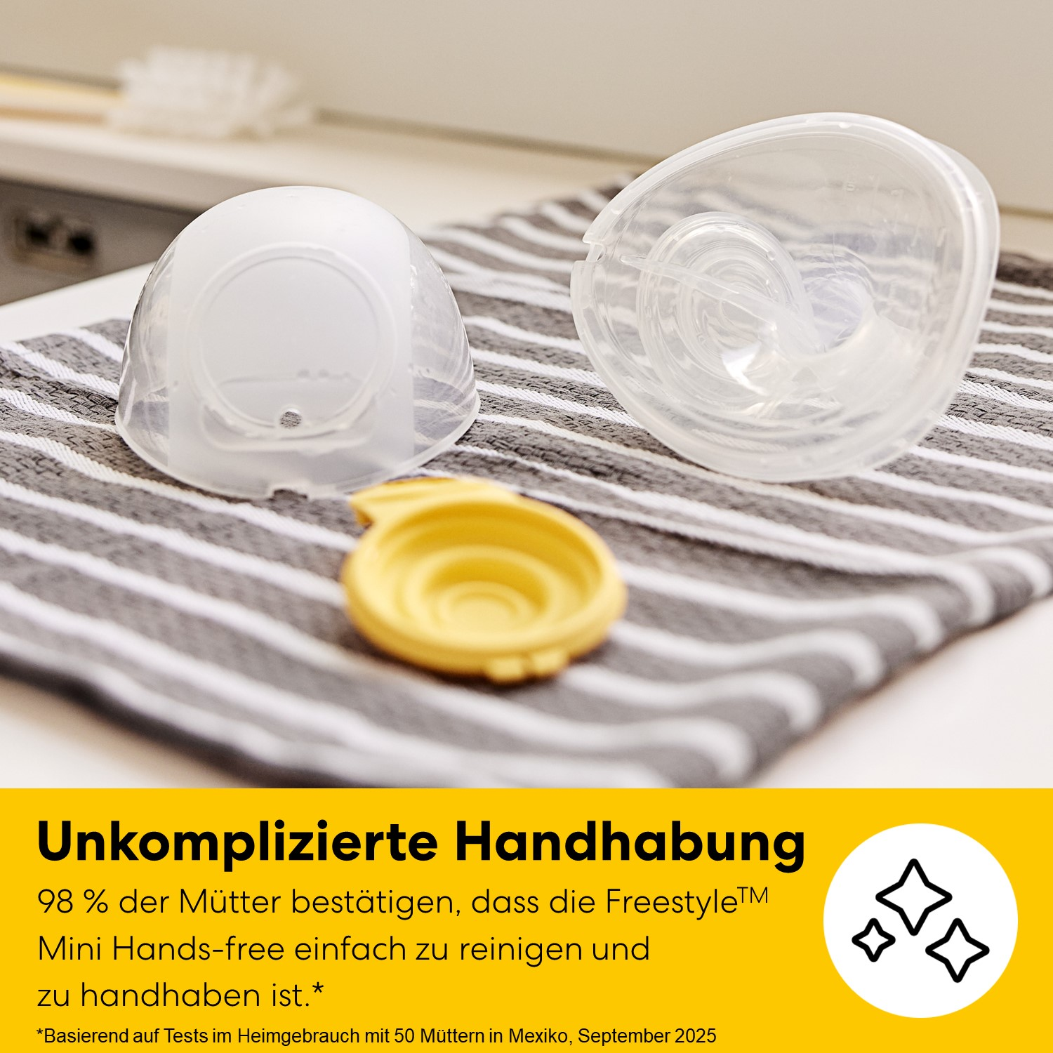Zwei durchsichtige Teile eines Milchpumpen-Sets liegen auf einem gestreiften Tuch.