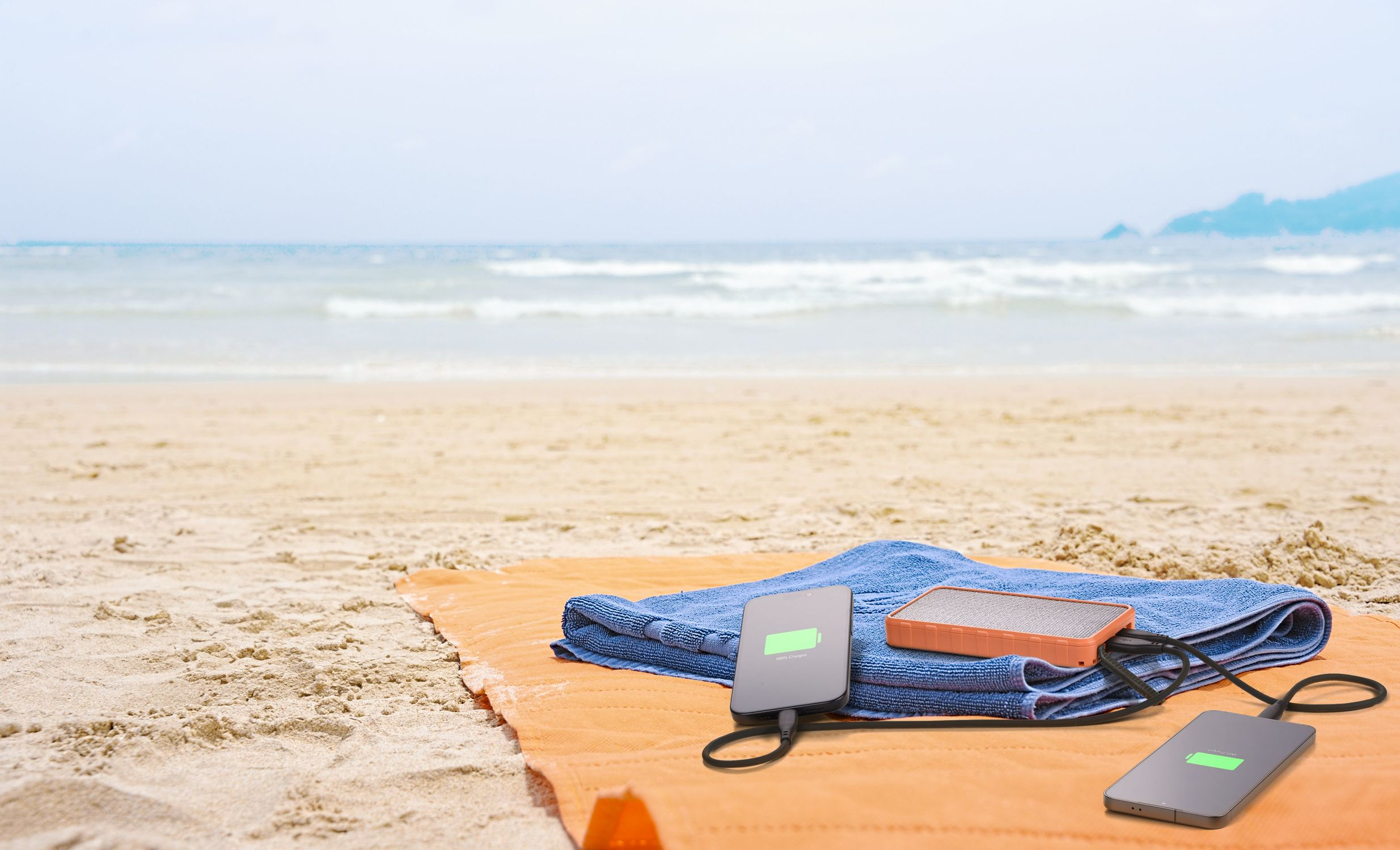 Serviette orange avec serviette bleue, téléphone et haut-parleur sur la plage.