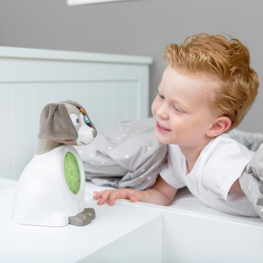 Un bambino dai capelli rossi è sdraiato a letto guardando una sveglia a forma di cane.