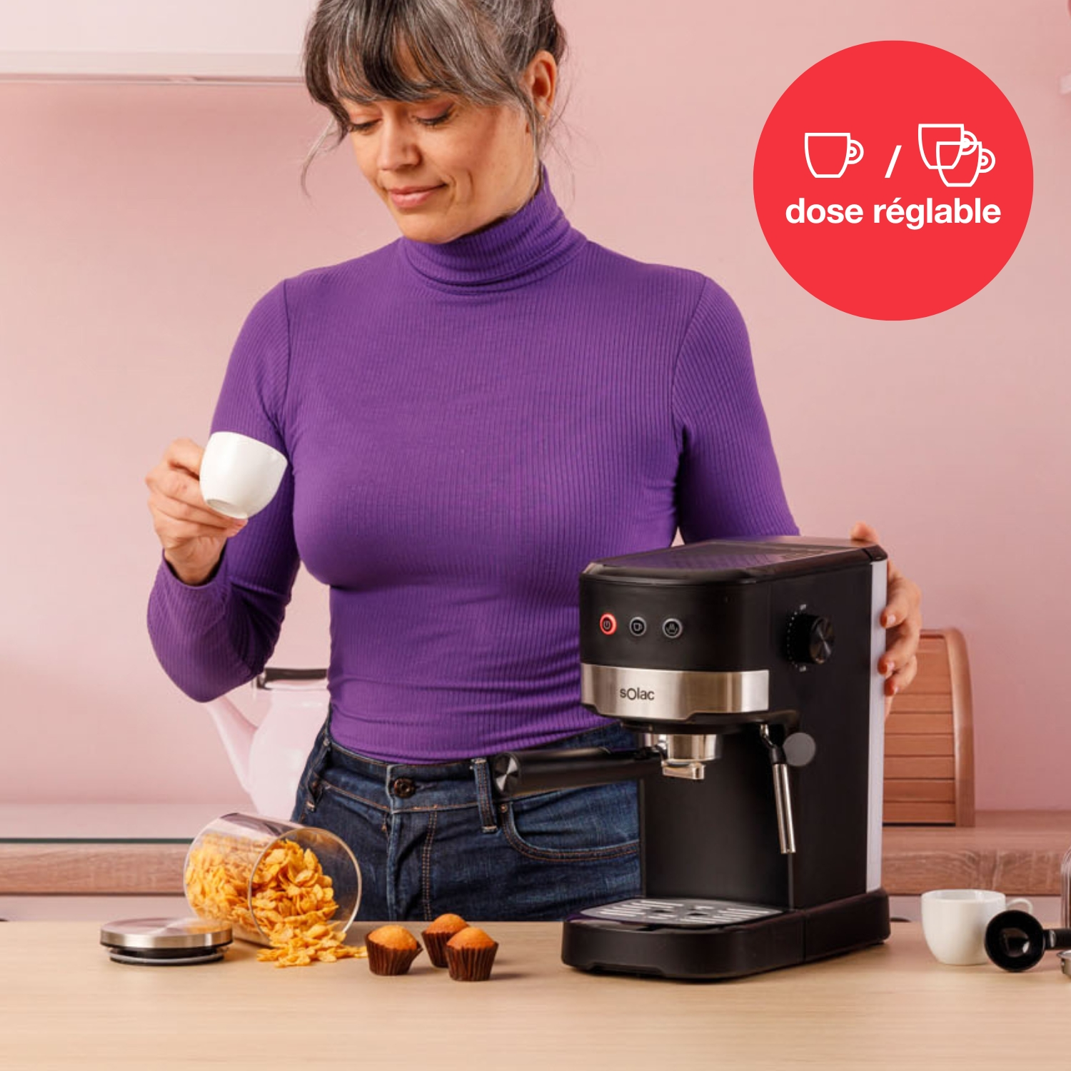 Mujer con jersey morado de cuello alto sostiene taza de café junto a cafetera.