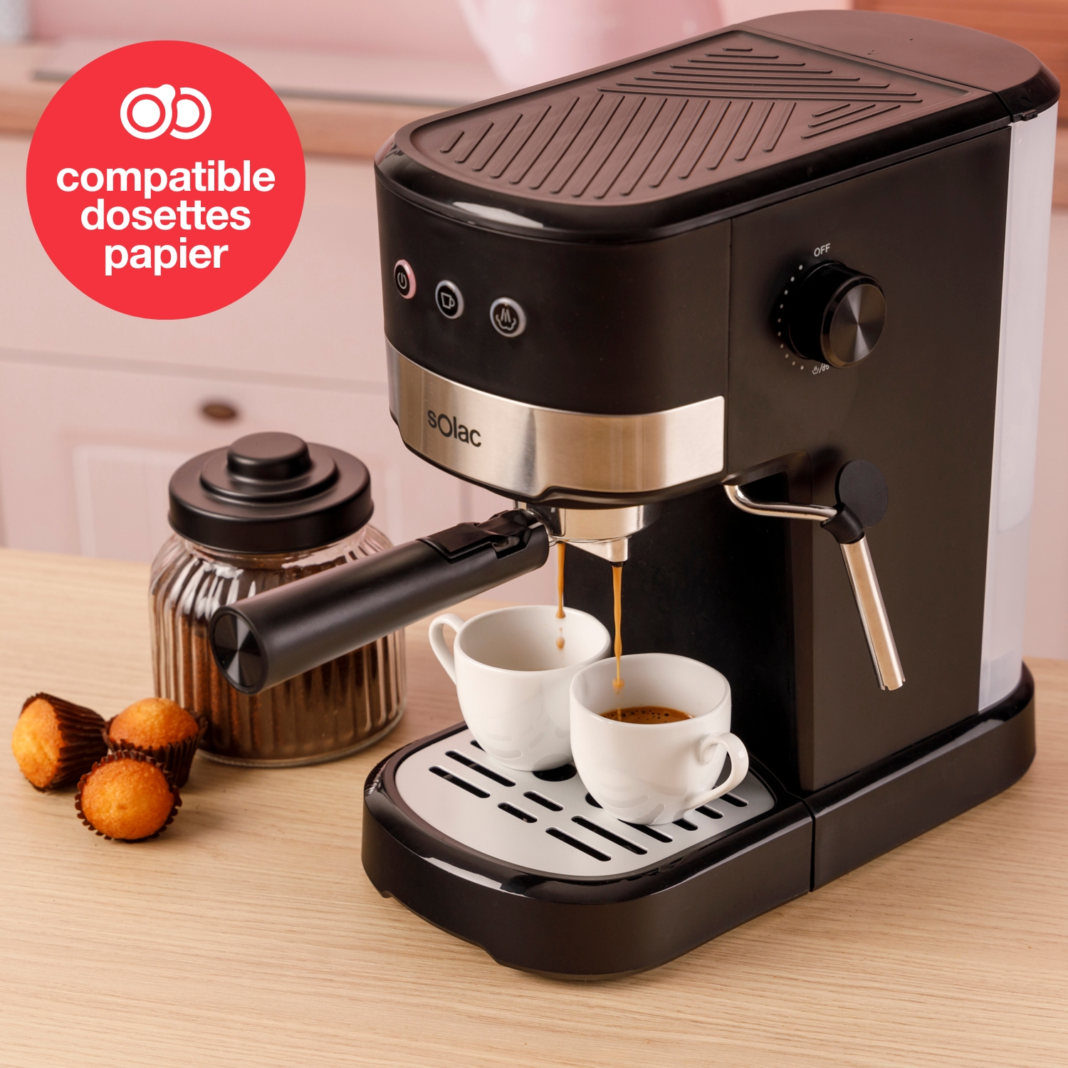 Una cafetera negra sirve espresso en dos tazas blancas. Al lado hay un tarro de café y magdalenas.
