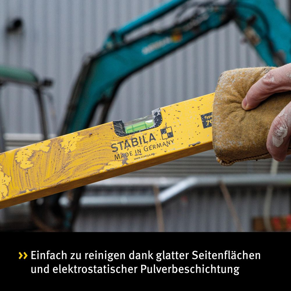Niveau à bulle jaune nettoyé avec une éponge marron. Machine de chantier en arrière-plan.