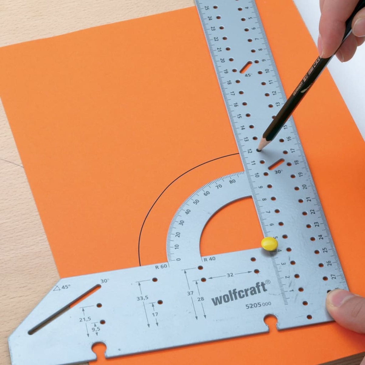 Una matita disegna su carta arancione usando un goniometro e un righello.