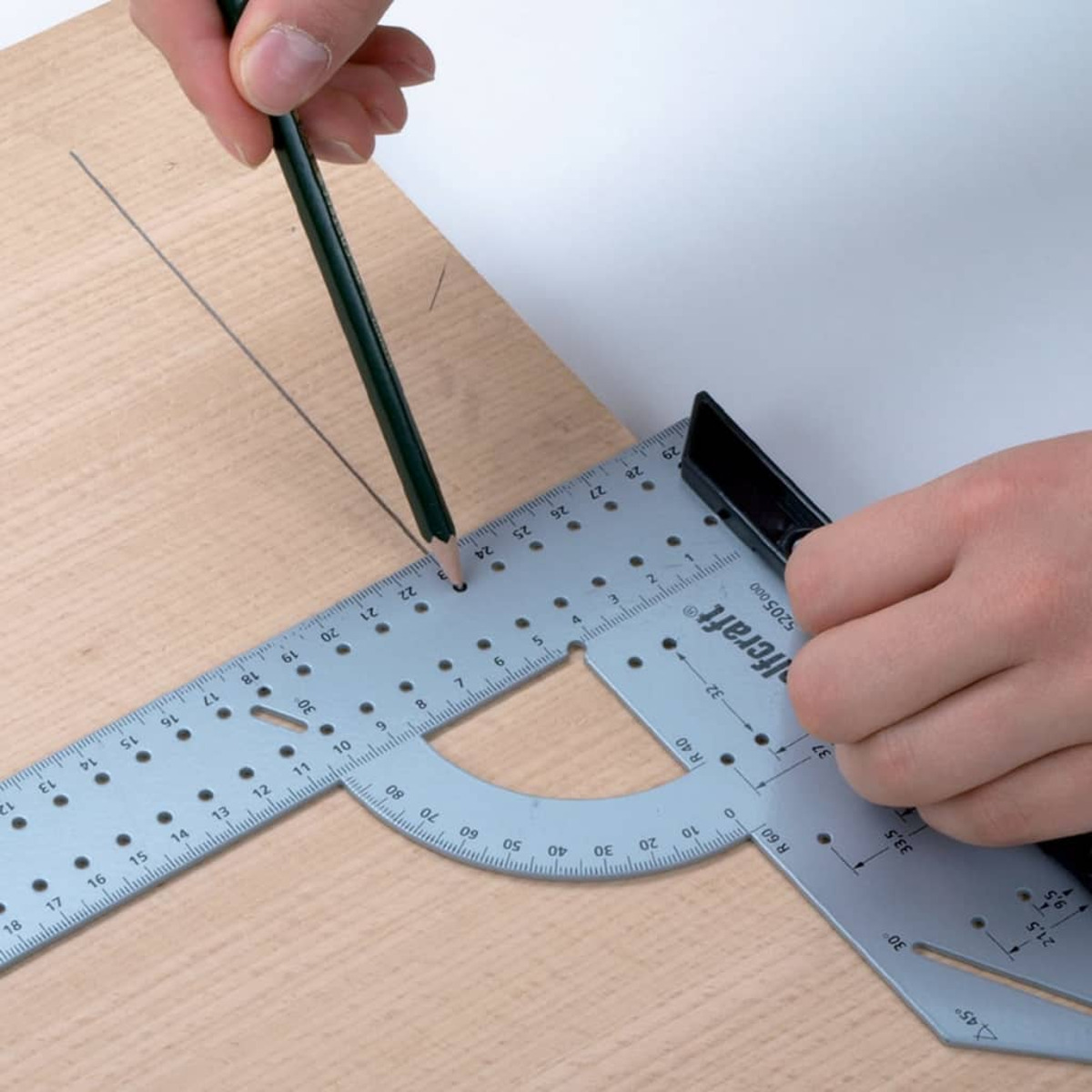 Una mano disegna una linea su legno con una matita e un righello goniometro.