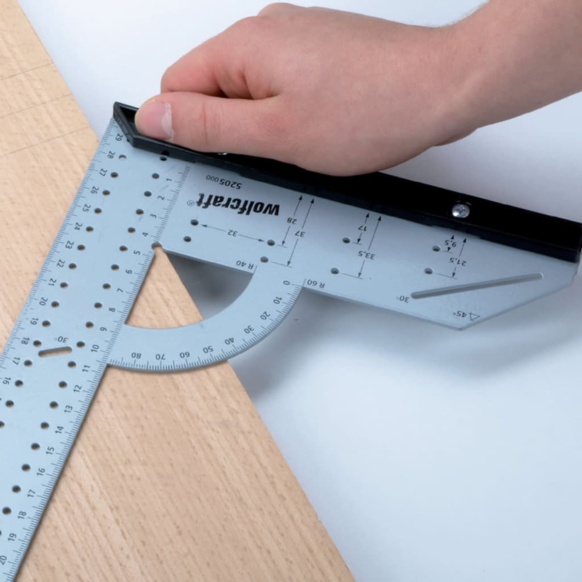 Una mano tiene una squadra combinata su una tavola di legno. L'utensile ha delle marcature.