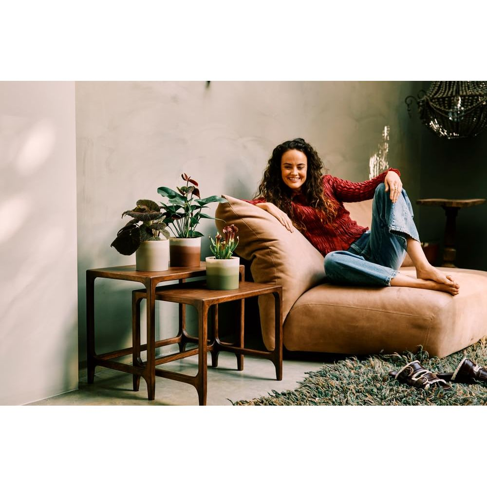 Frau auf einem braunen Sofa, mit Pflanzen auf einem Holztisch daneben.