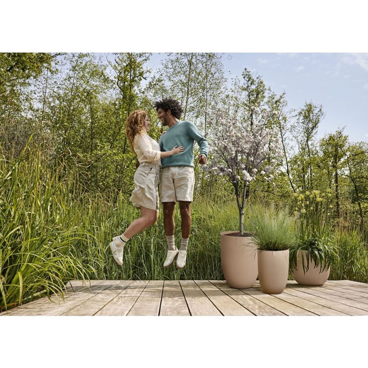 Ein Paar springt auf einer Holzterrasse im Freien, umgeben von üppiger Vegetation.