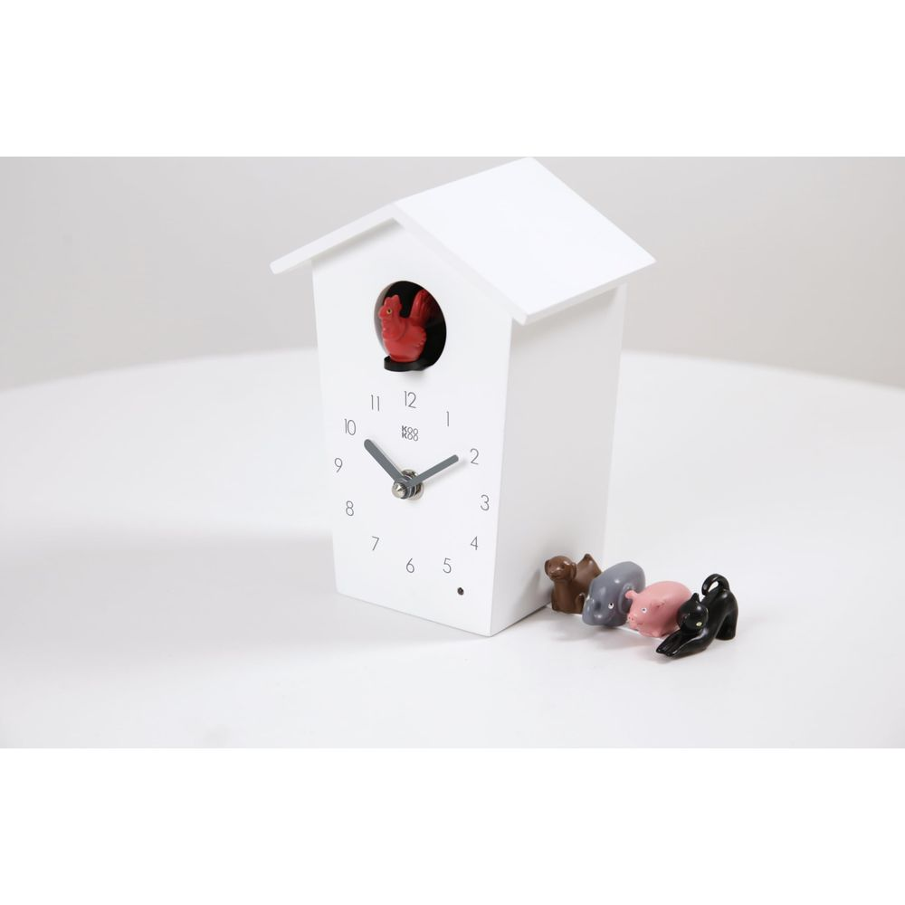 Un coucou blanc avec un oiseau rouge et trois petites figurines d'animaux devant.