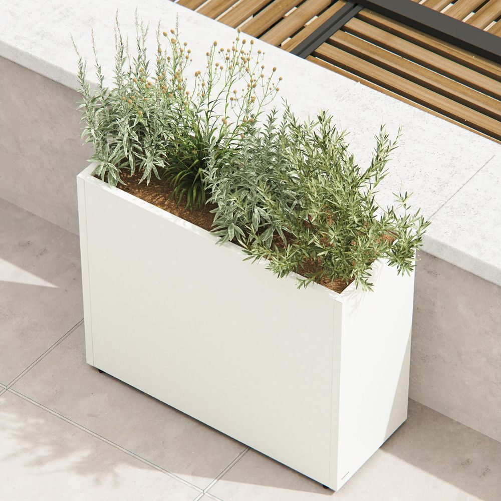 Ein weißer rechteckiger Pflanzkasten mit grünen Pflanzen auf einer grauen gefliesten Terrasse.