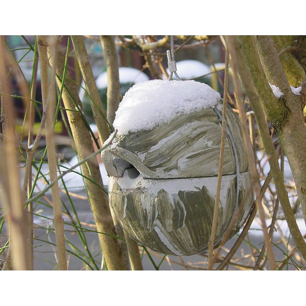 Ein getarnter Ball, bedeckt mit Schnee, hängt an einem Draht zwischen kahlen Ästen.