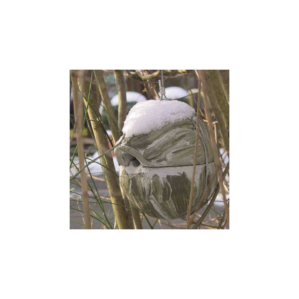 Ein graues, strukturiertes Vogelhaus mit Schnee darauf hängt an Ästen.