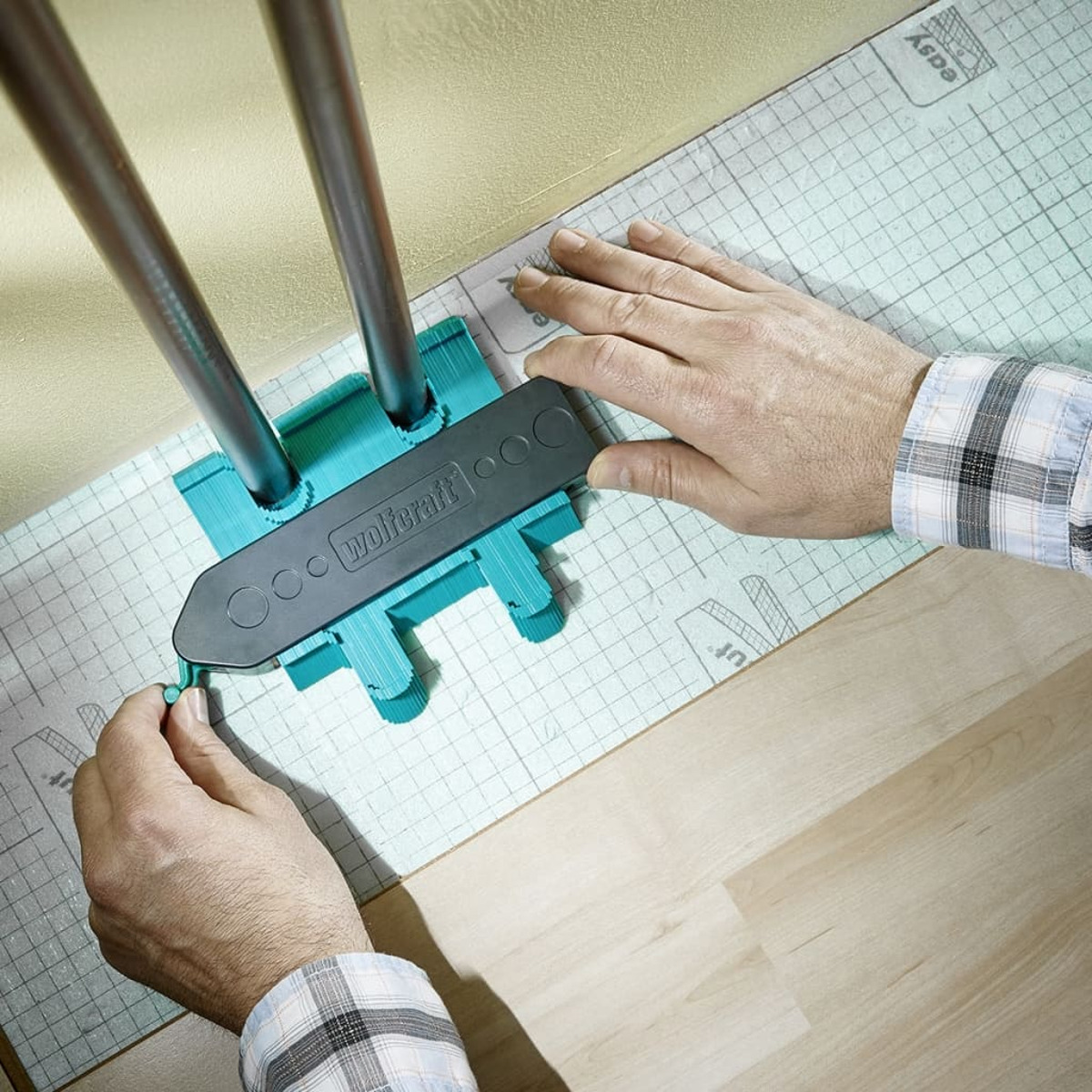 Un uomo usa un calibro di contorno per tracciare la forma dei tubi sul materiale del pavimento.