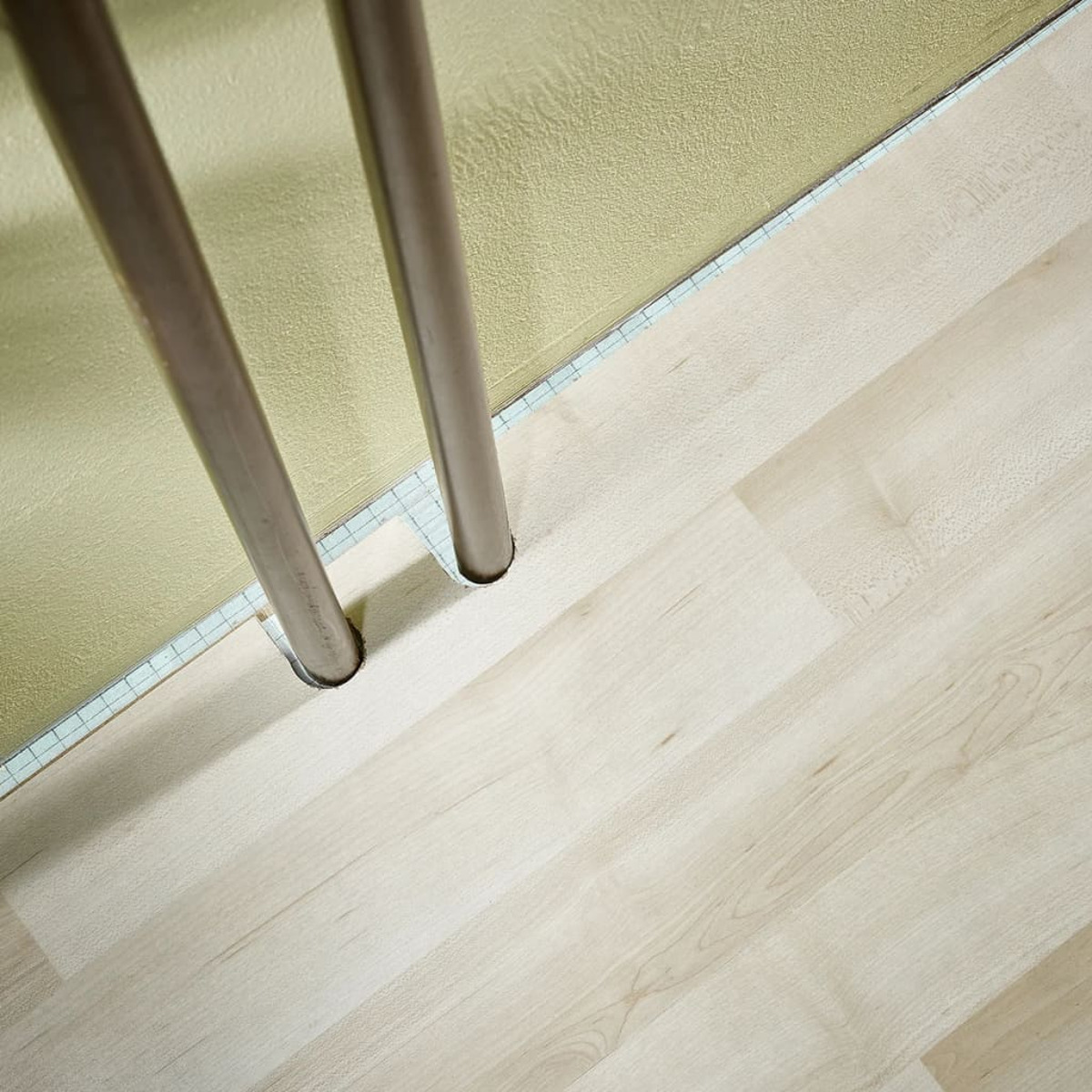 Due tubi metallici su un pavimento in legno chiaro davanti a una parete gialla.