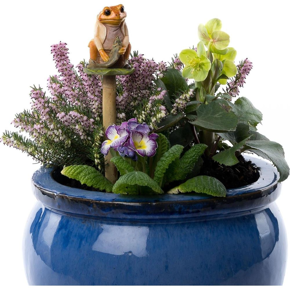 Eine Froschfigur sitzt auf einer Pflanze in einem blauen Topf mit lila und rosa Blumen.
