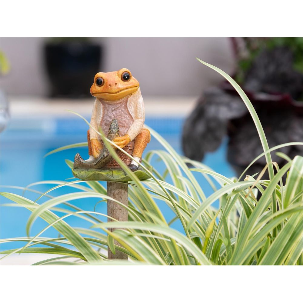 Eine Gartendekoration eines Frosches, der auf einem Blatt sitzt, im Vordergrund sind Pflanzen.