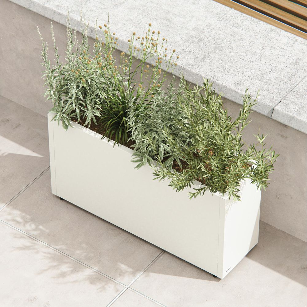 Ein weißer Pflanzkasten mit grünen Pflanzen und einigen gelben Blüten auf einer gefliesten Terrasse.