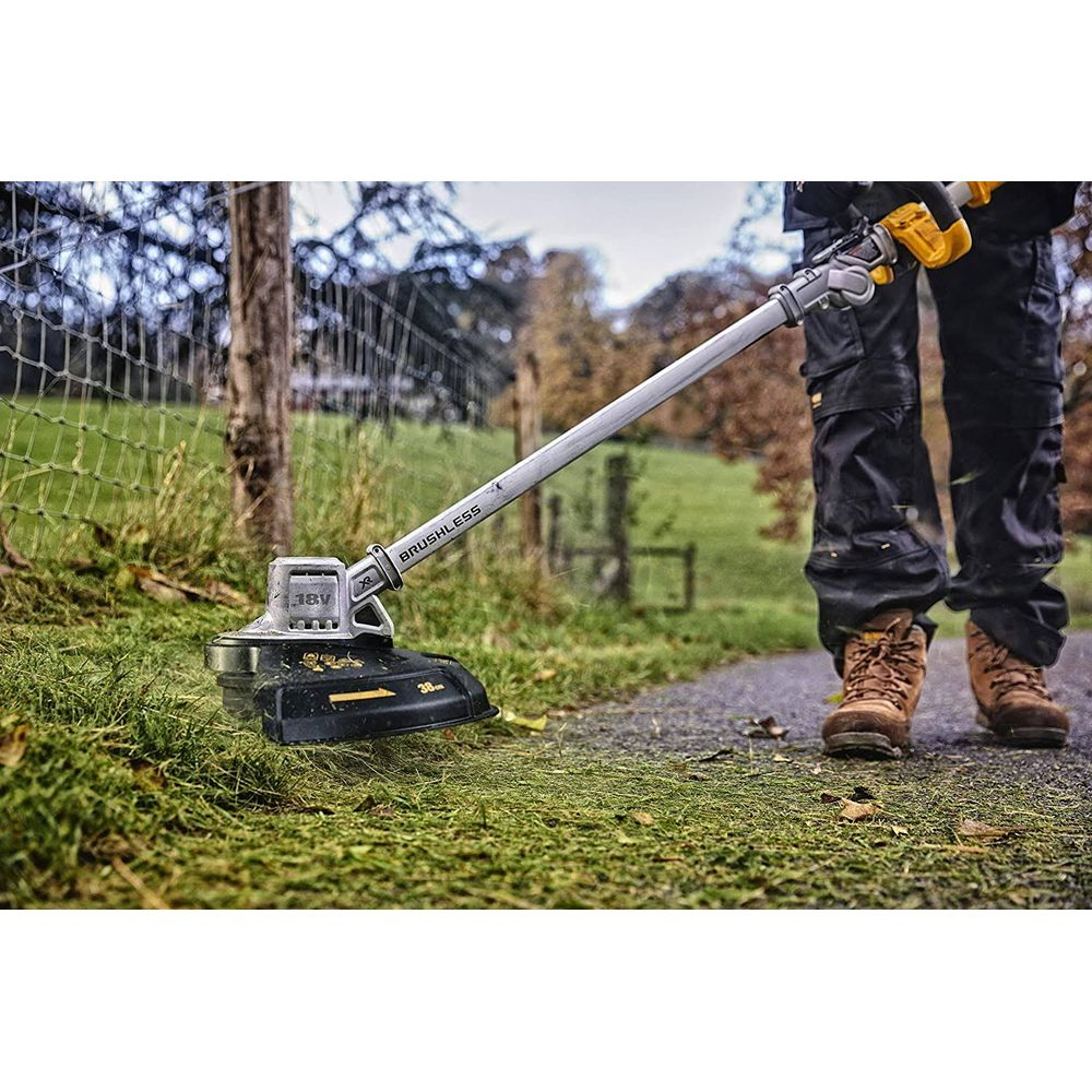 Ein Mann mit Arbeitskleidung trimmt Gras mit einem kabellosen Rasentrimmer.
