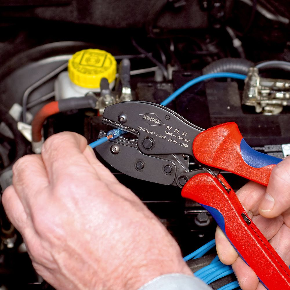 Eine Person benutzt eine rote und blaue Zange, um ein blaues Kabel im Motorraum eines Autos zu crimpen.