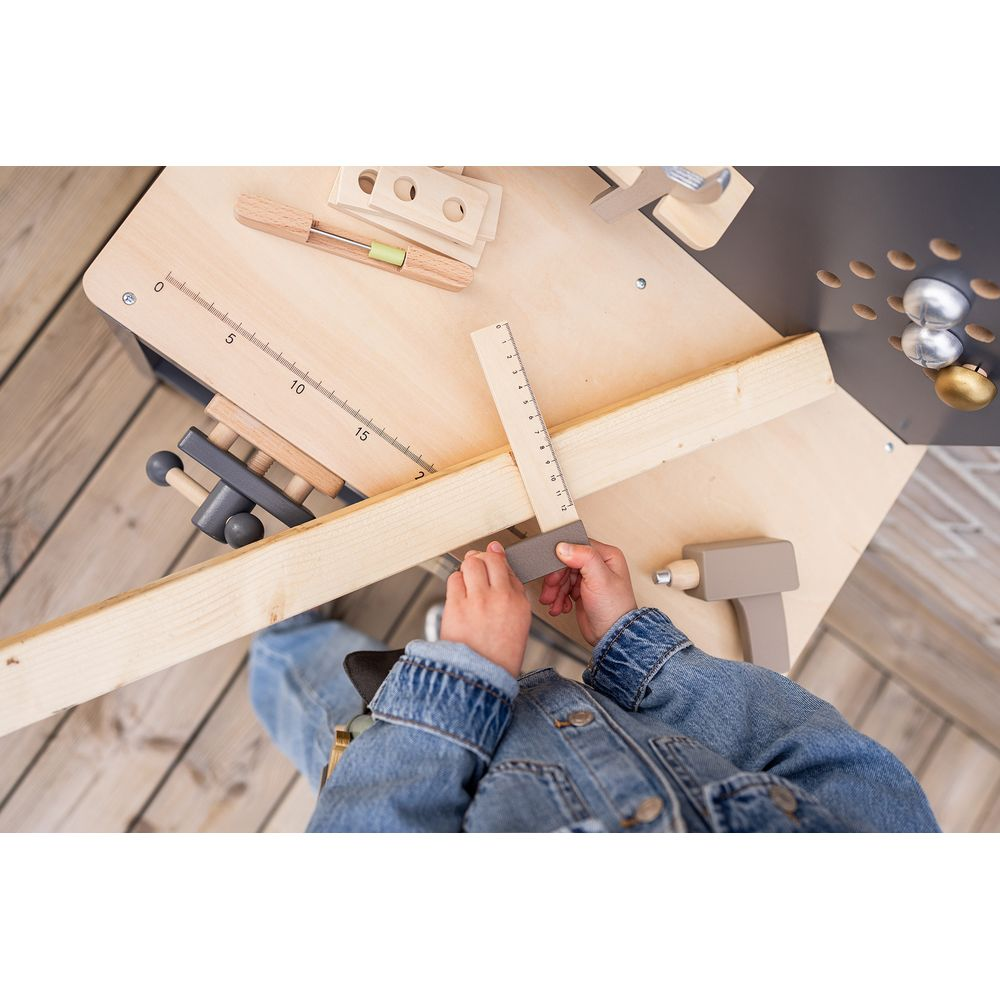 Kind mit Jeansjacke spielt mit Holzwerkzeugen, misst Holz mit Lineal.