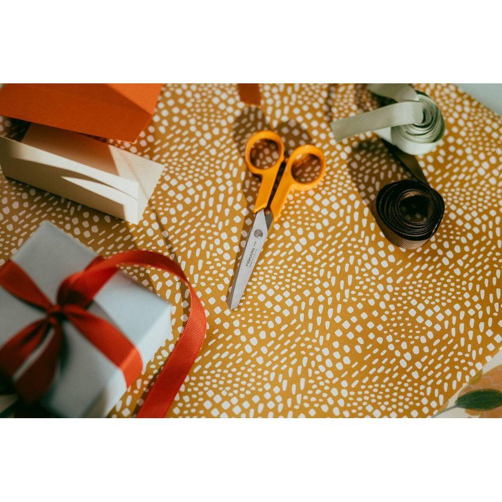 Schere mit orangefarbenem Griff auf gelbem Tupfenpapier mit Geschenk, Band und orangefarbener Karte.