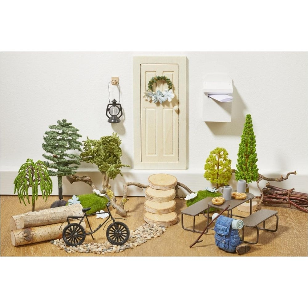 Scena di giardino in miniatura con porta, tavolo, bicicletta, zaino e alberi.