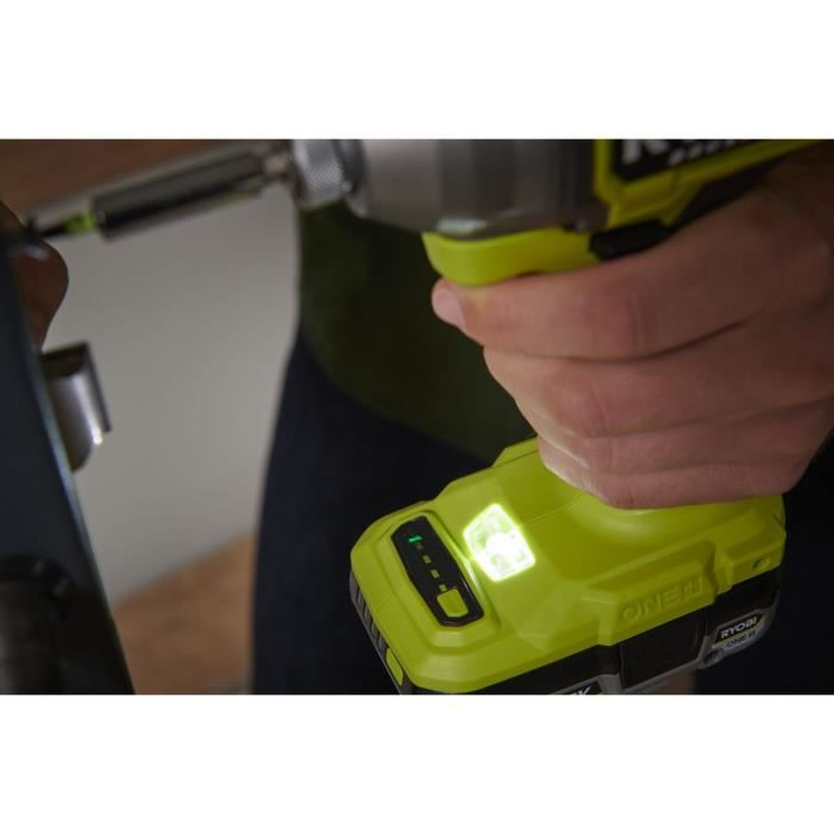 Eine Hand hält einen grünen Ryobi-Bohrer mit beleuchtetem Akku und Indikatoren.