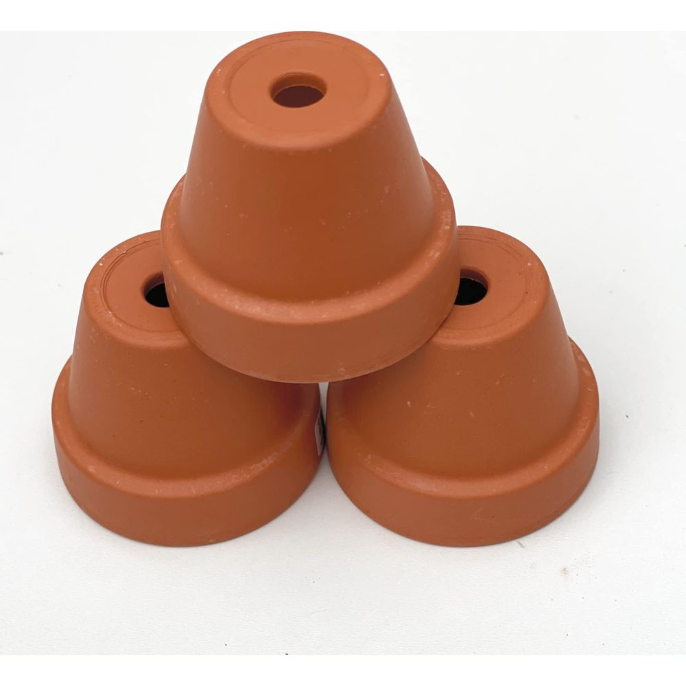 Trois petits pots de fleurs en terre cuite empilés sur fond blanc.