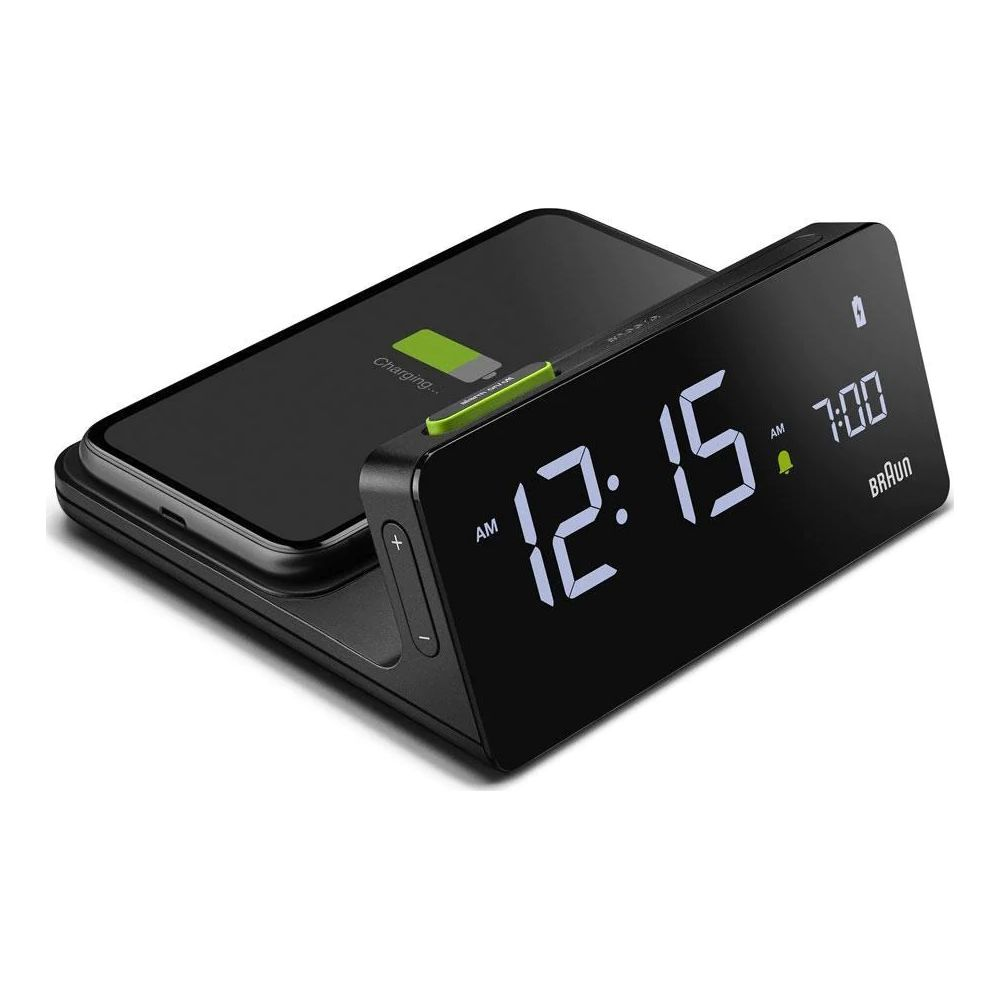 Ein schwarzes Smartphone wird auf einer Ladestation geladen, daneben ein digitaler Wecker mit der Anzeige 12:15.