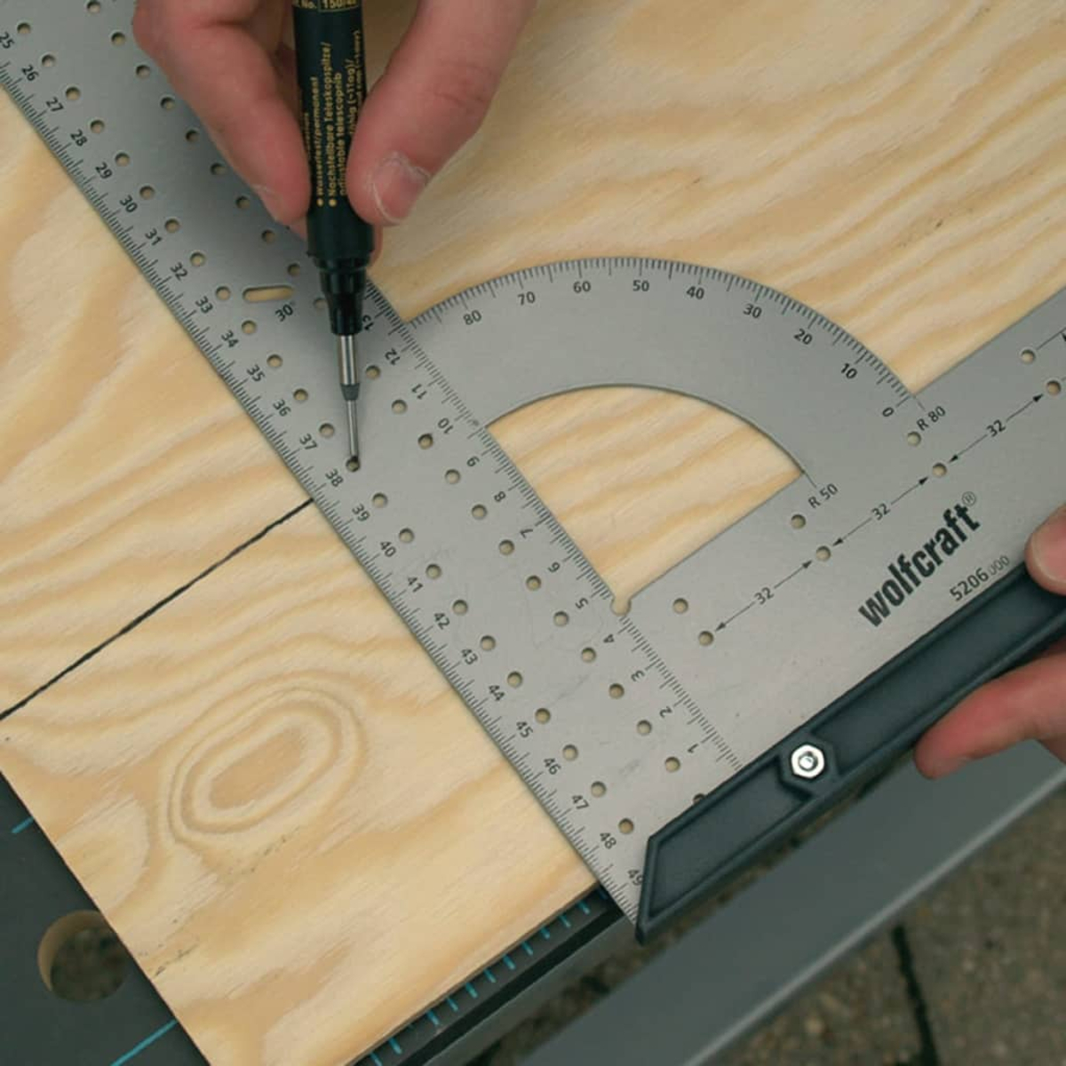 Ein Stift markiert eine Linie auf Holz mit einem Winkelmesser und Lineal.
