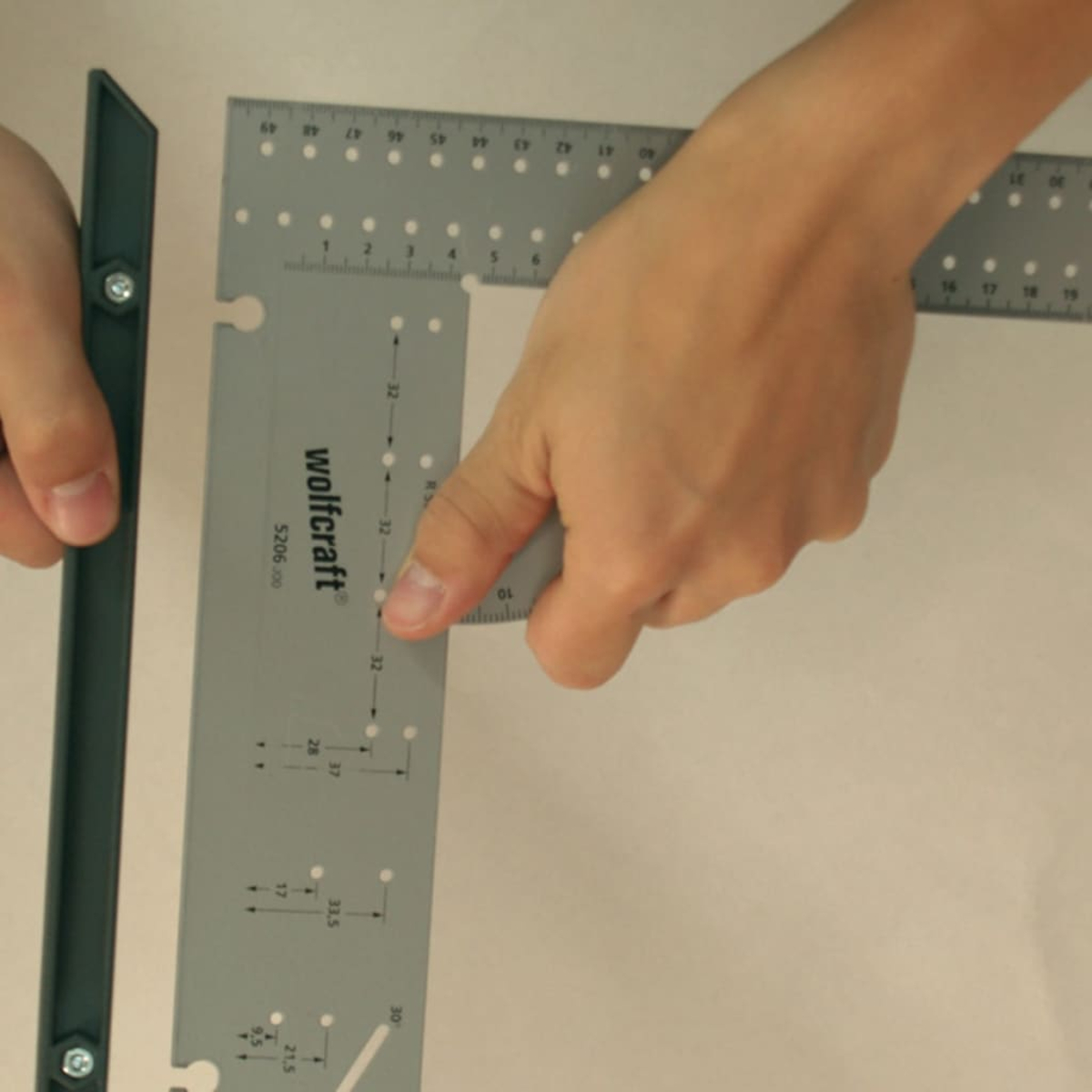 Eine Hand hält ein graues Winkelmaß mit Markierungen und Zahlen.