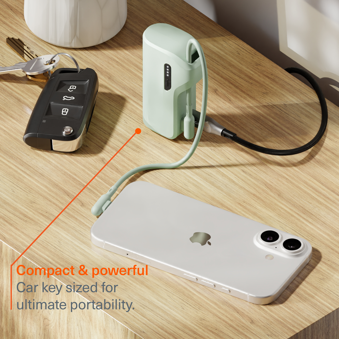 Ein mintgrüner Akku lädt ein weißes Smartphone neben einem Autoschlüssel auf einem Holztisch.