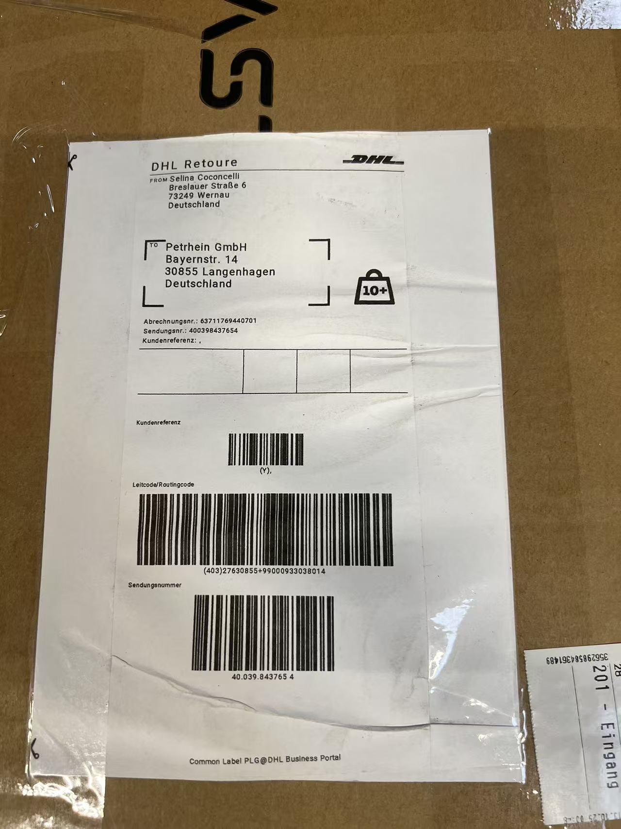 DHL Retoure-Etikett mit Absender-, Empfängeradresse und Barcodes auf braunem Karton.