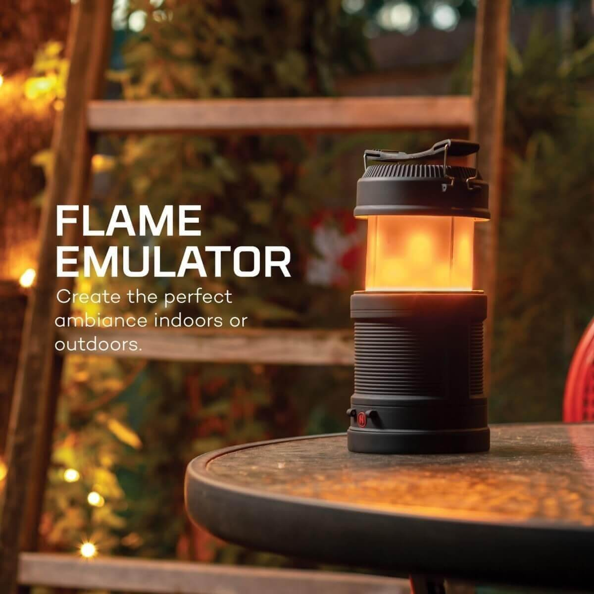 Une lanterne noire à lumière orange vacillante est posée sur une table en extérieur.