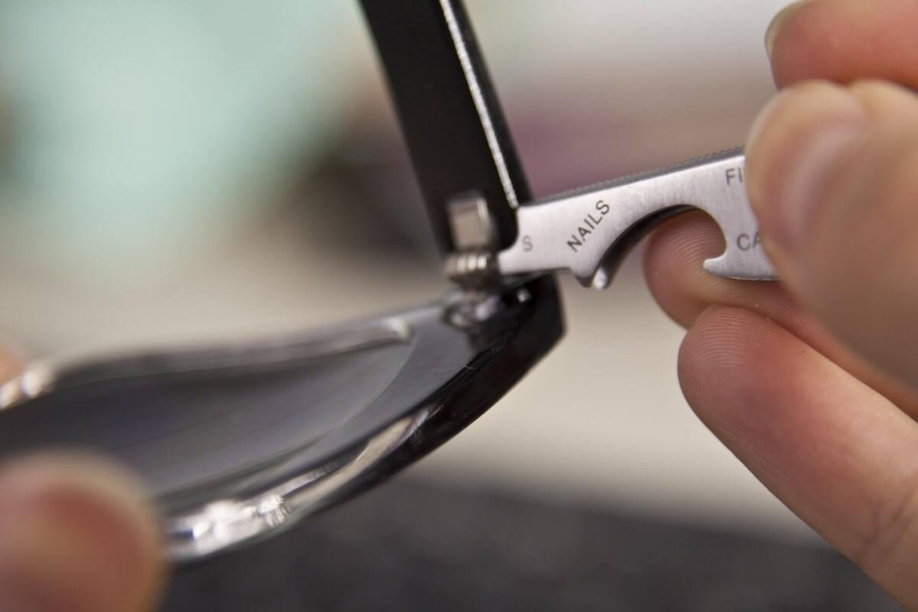 Eine Hand hält ein Multitool an einer Brille.