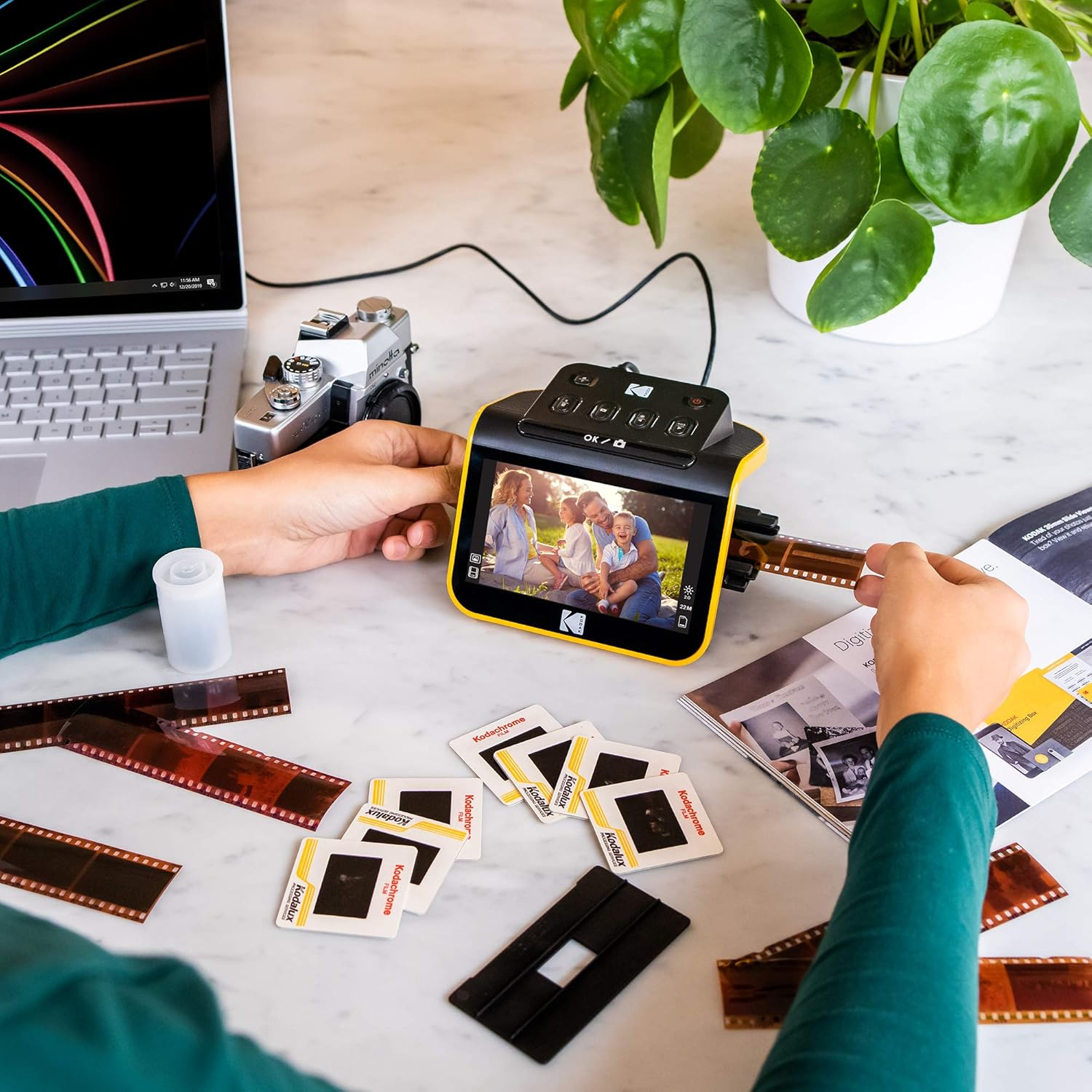 Eine Person digitalisiert Film mit einem Kodak-Scanner, Laptop und Vintage-Kamera.
