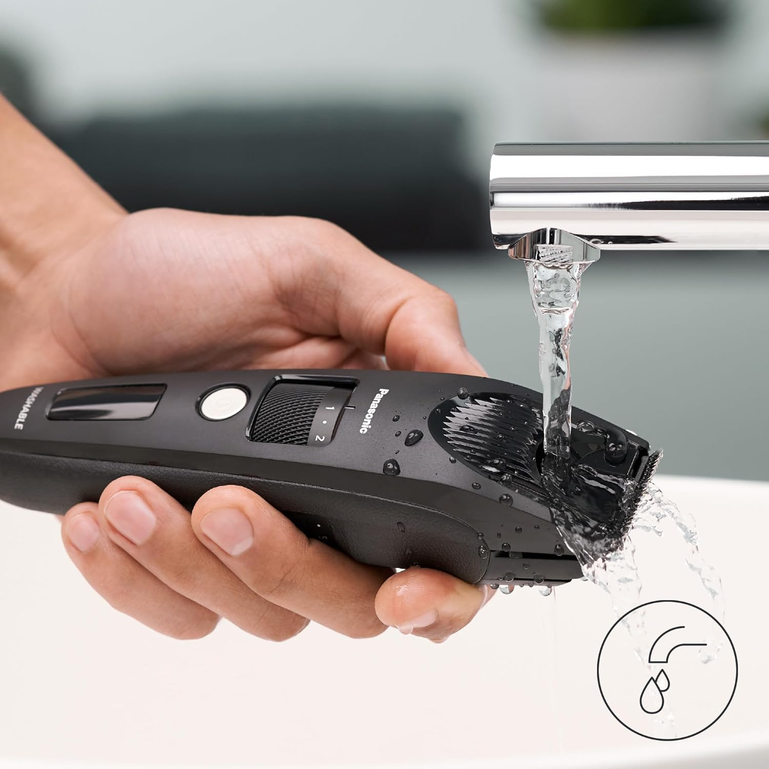 Ręka trzyma czarną maszynkę Panasonic pod bieżącą wodą z kranu.