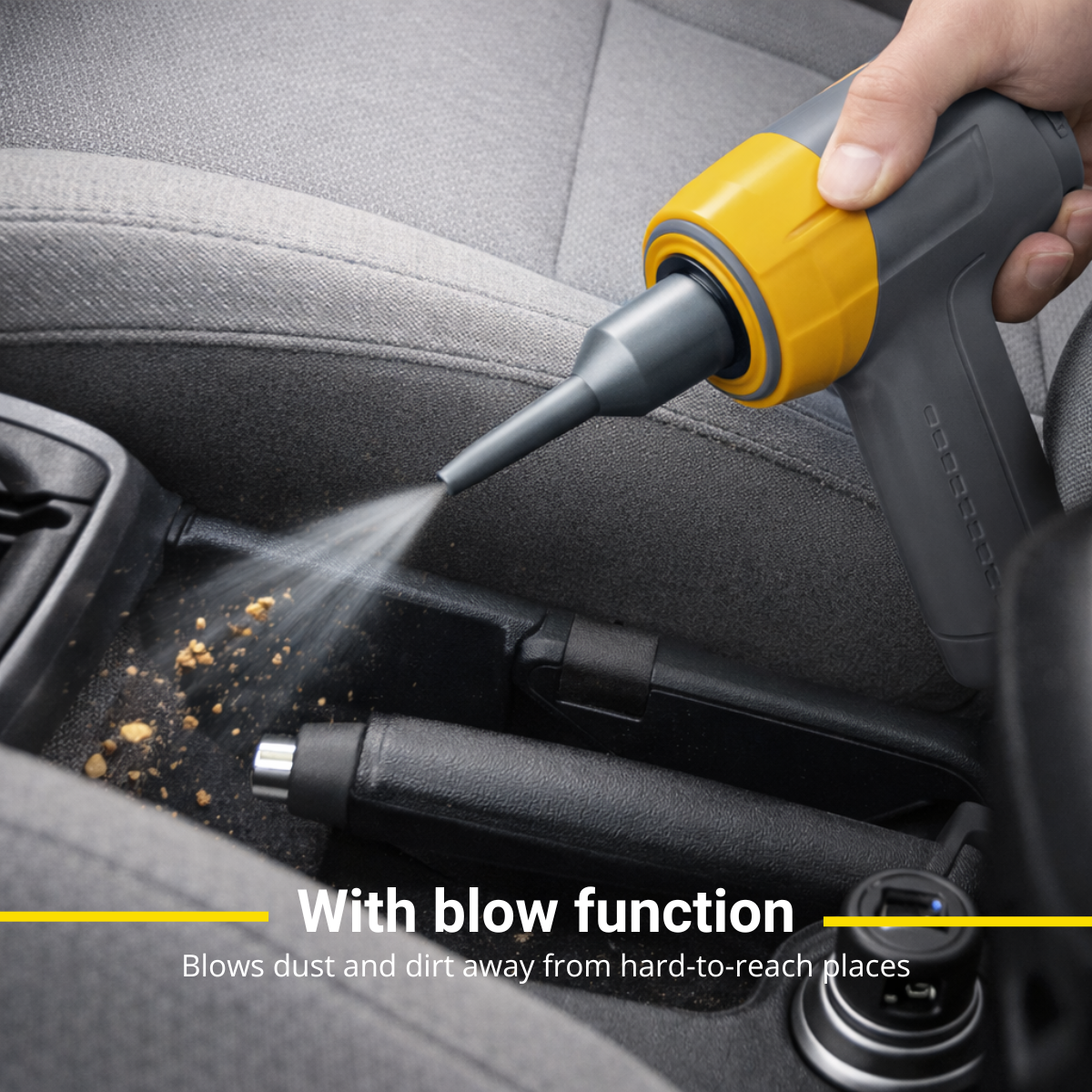 Une main utilise un appareil gris et jaune pour souffler la poussière de la console d'une voiture.