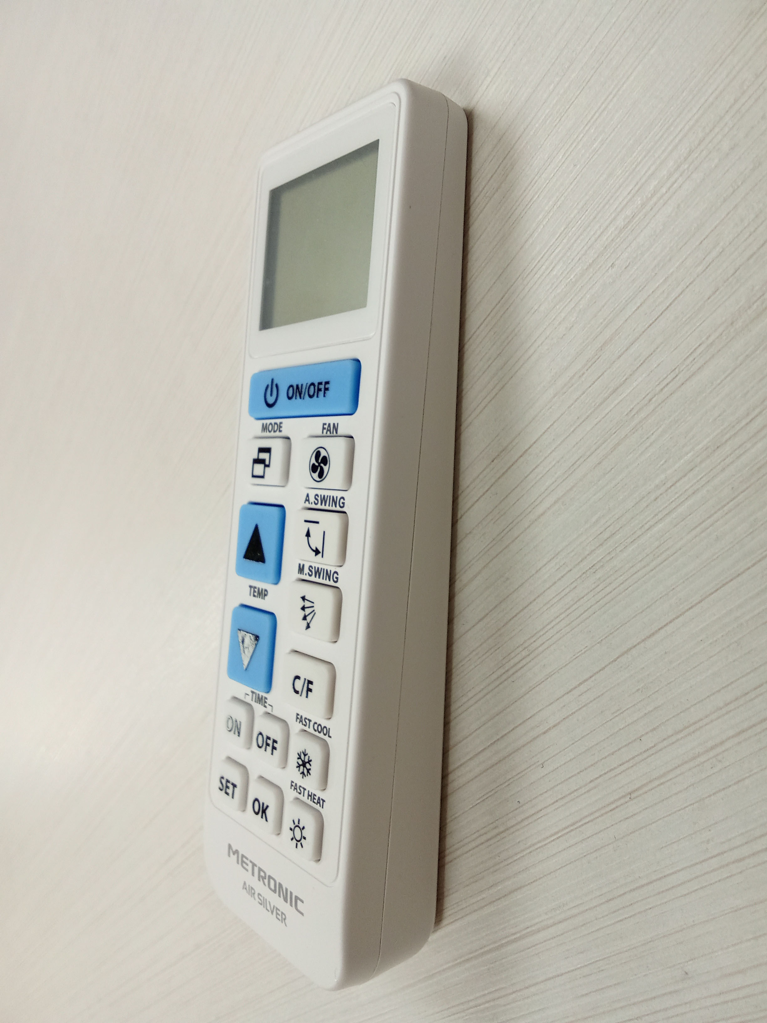 Mando a distancia blanco con botones de aire acondicionado, sobre fondo de madera.