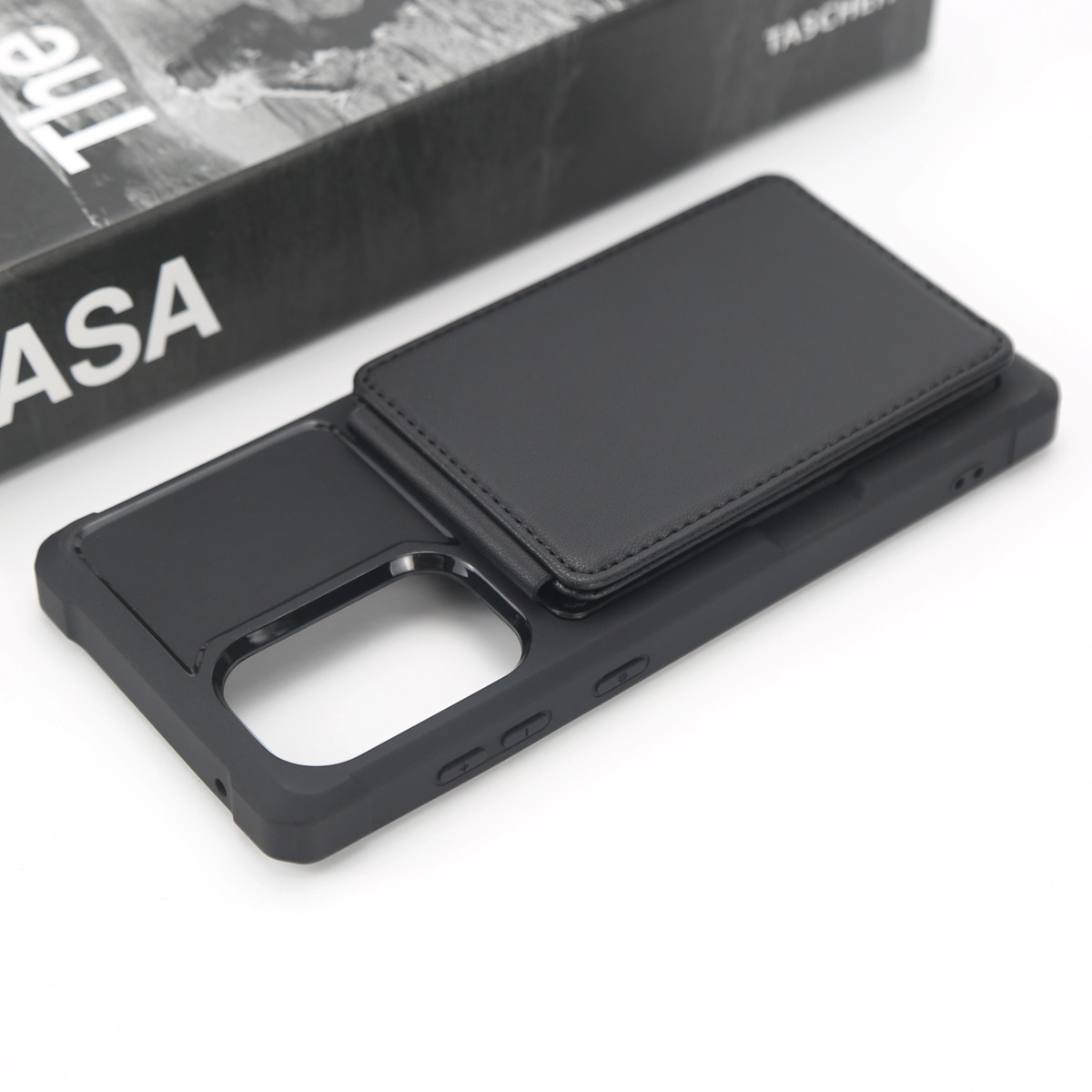 Custodia nera per telefono con porta carte su superficie bianca, accanto a un libro.