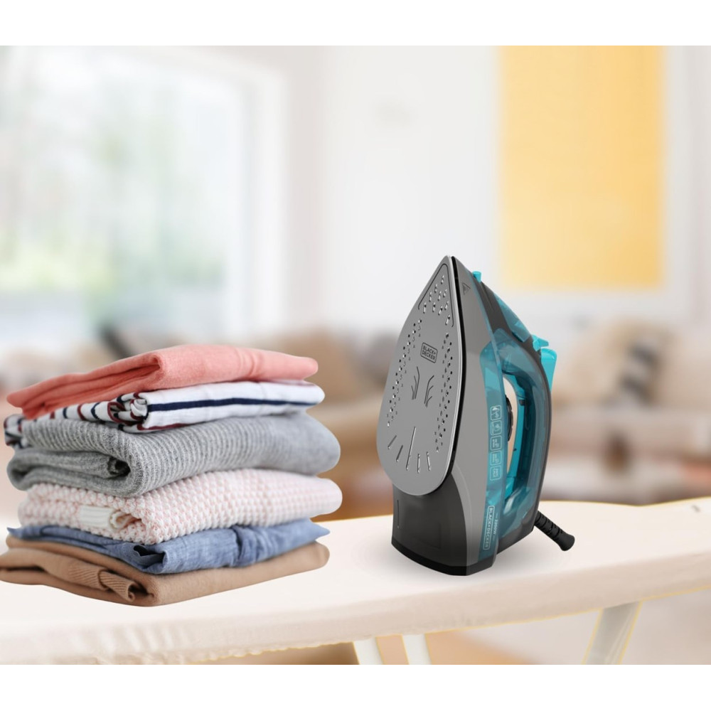 Żelazko obok stosu ubrań na desce do prasowania.