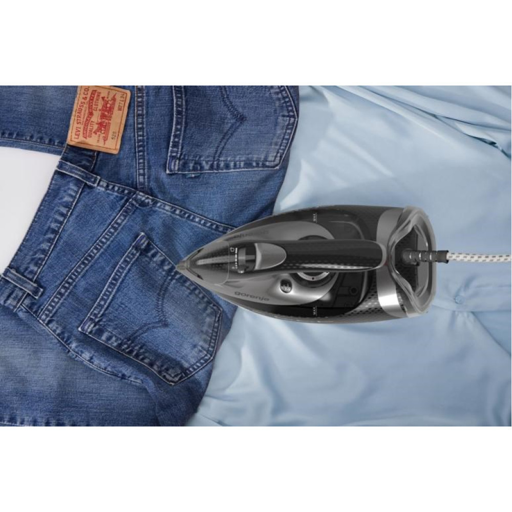 Un ferro da stiro nero su una camicia azzurra accanto a jeans.