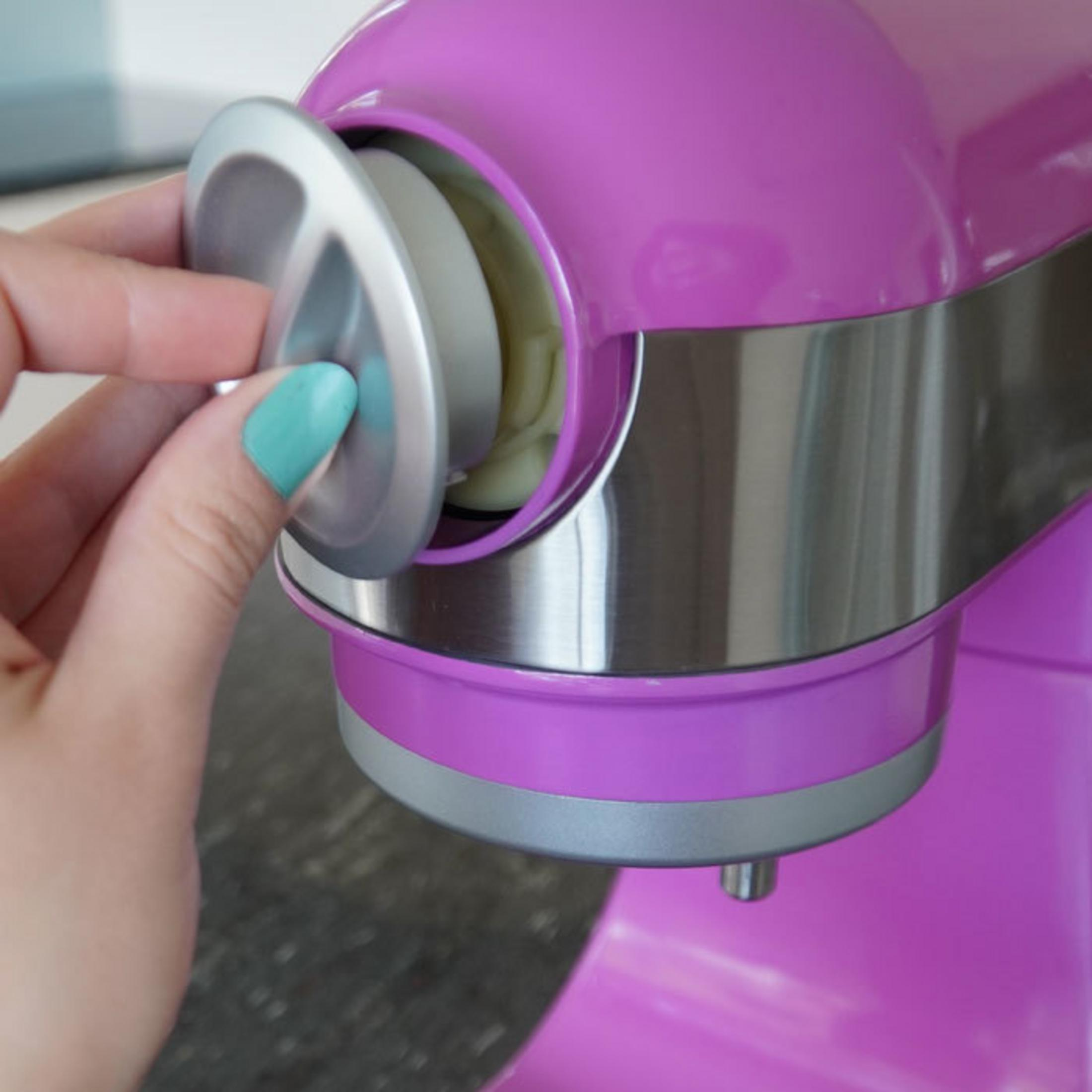 Mano apre uno sportello su un robot da cucina viola, rivelando contenuto cremoso.
