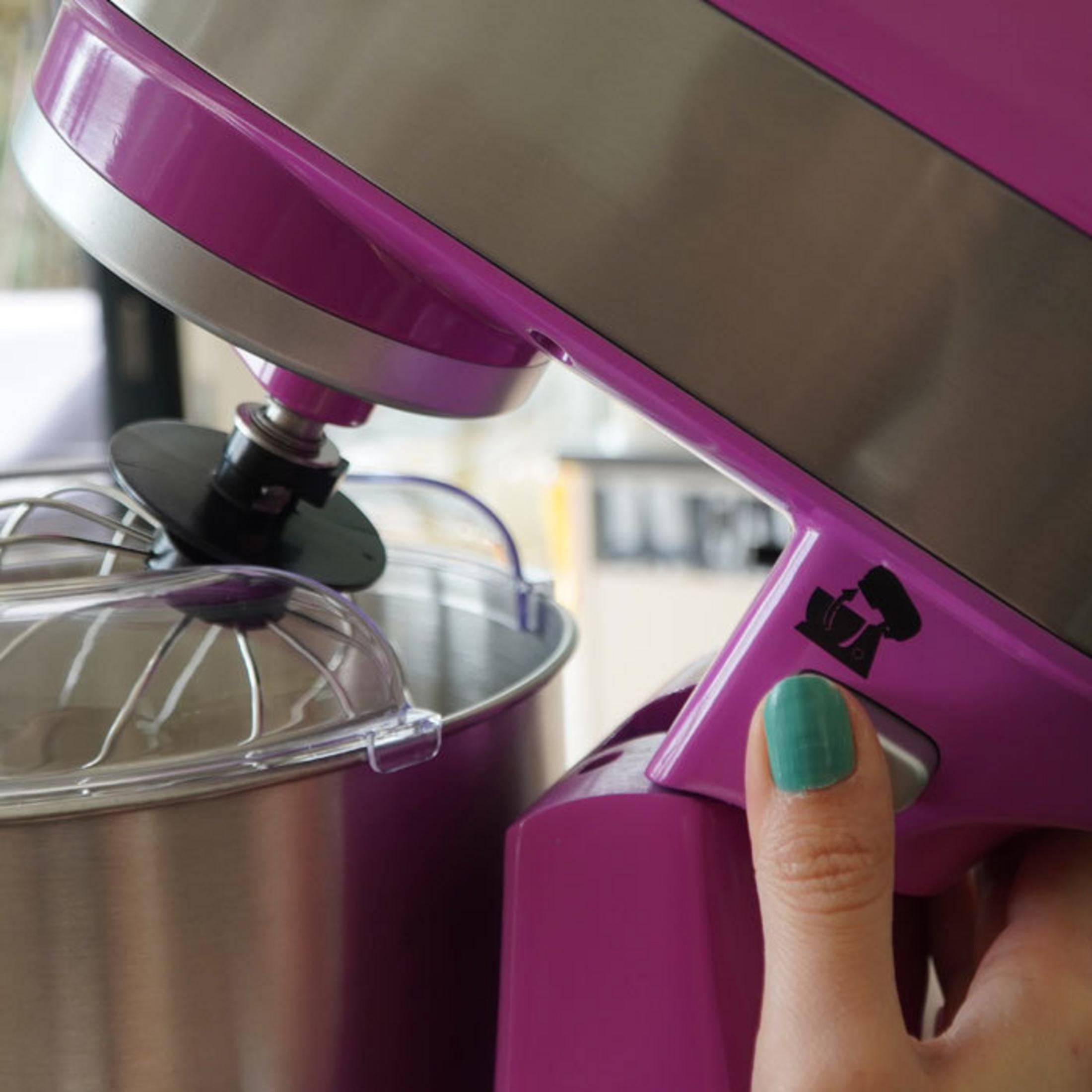 Una mano preme un pulsante su un'impastatrice viola con ciotola in acciaio.