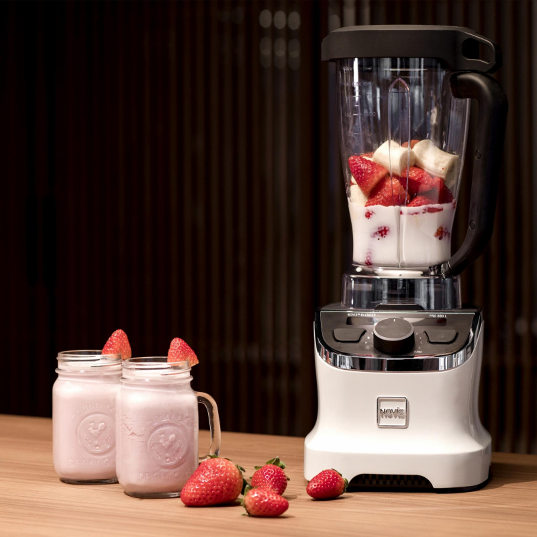 Ein weißer Mixer mit Erdbeeren und Bananen, daneben zwei Gläser Smoothie.