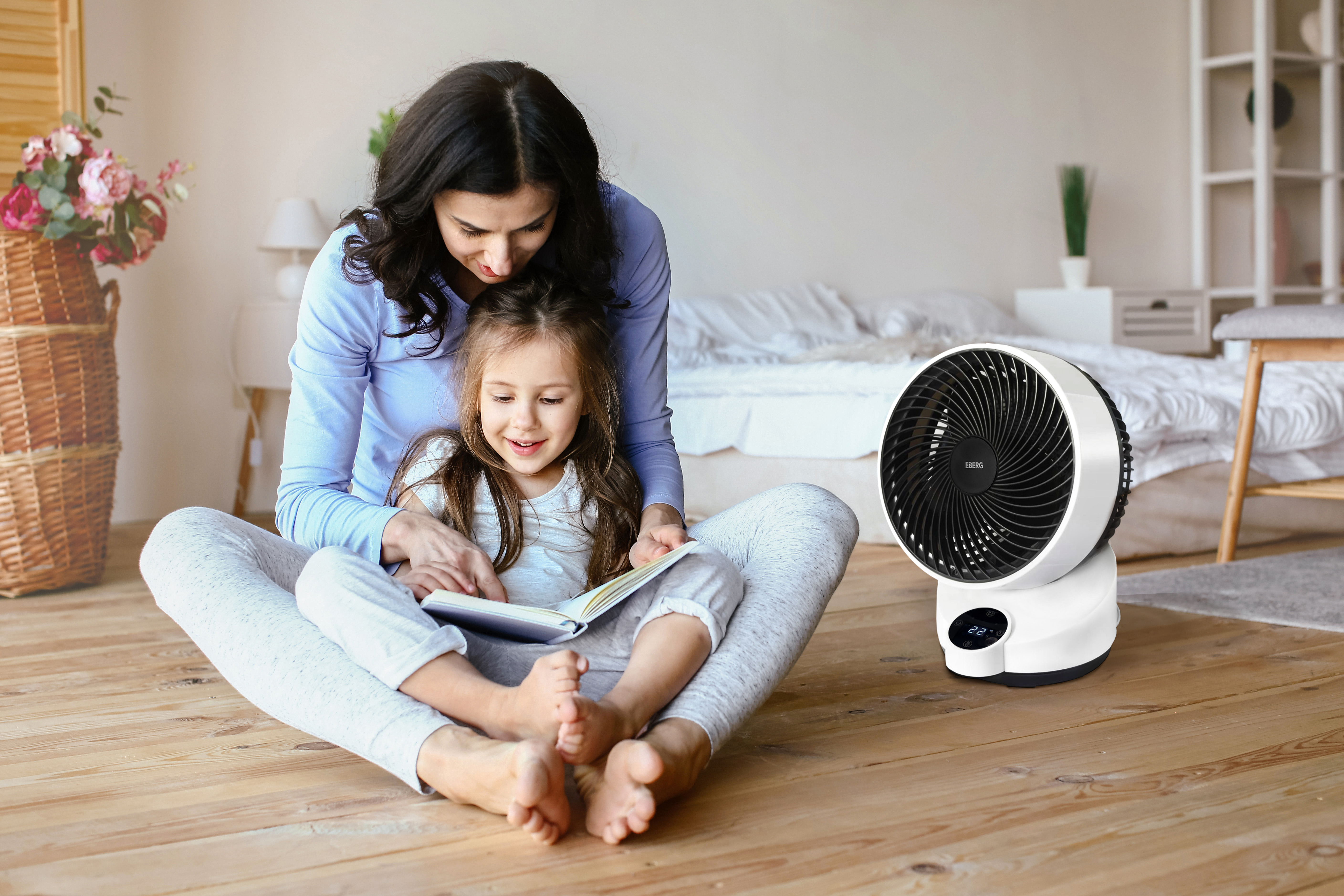 Matka i córka czytają książkę na podłodze. W pobliżu znajduje się biały wentylator.