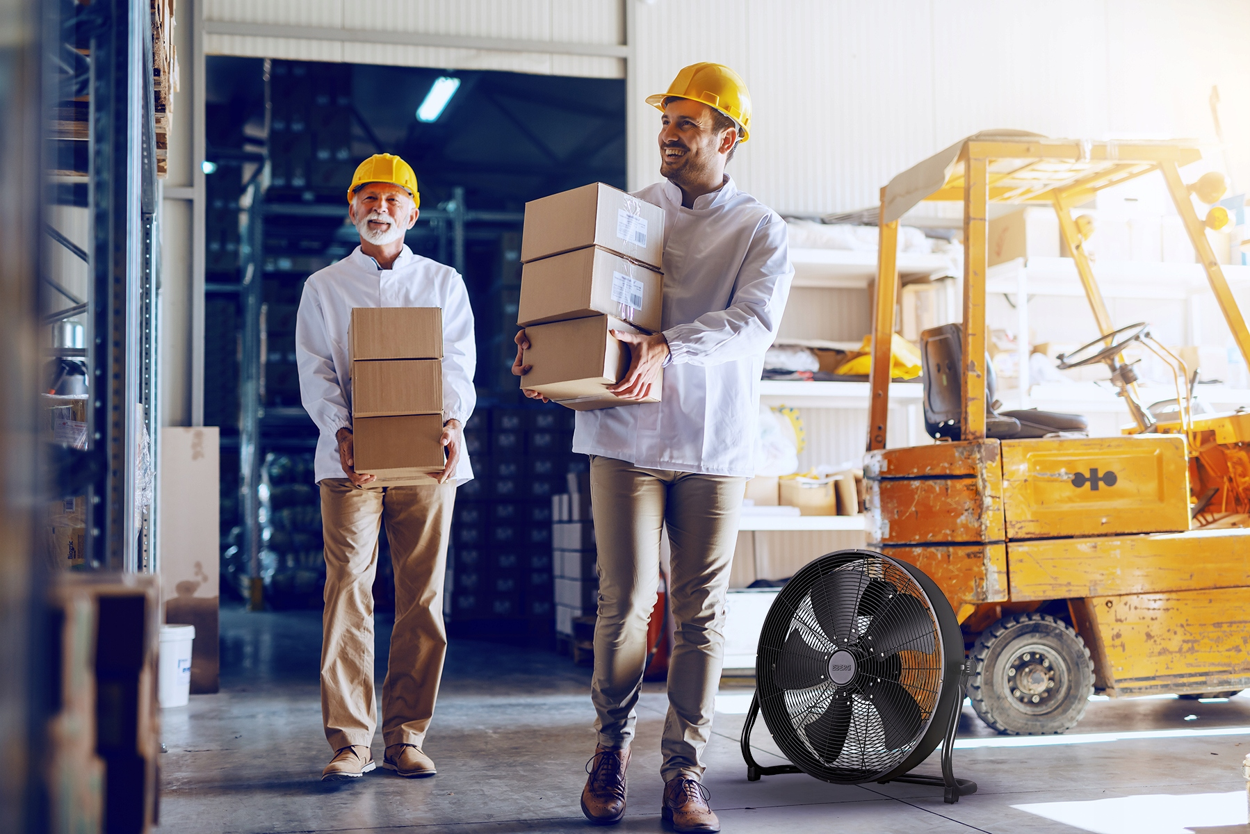 Dwóch mężczyzn w kaskach niesie pudełka w magazynie obok wózka widłowego.
