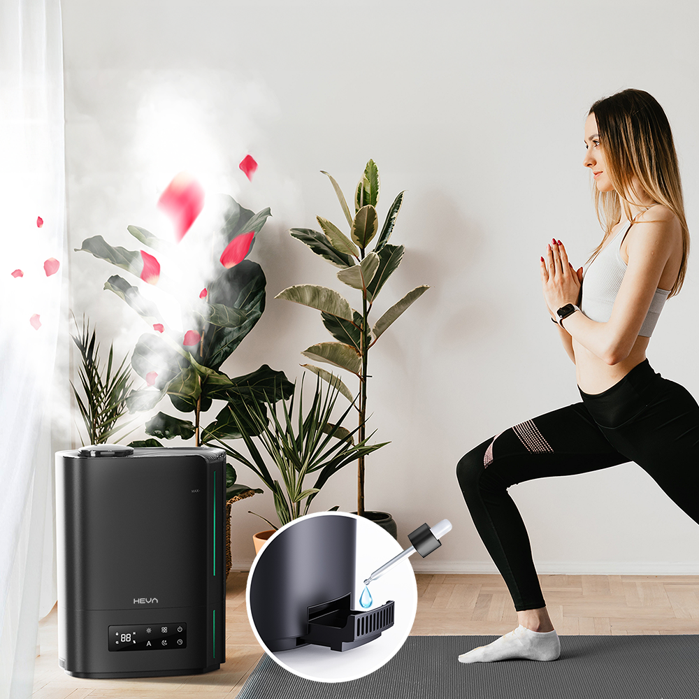 Kobieta ćwiczy jogę obok czarnego nawilżacza, z którego wydobywa się mgła i płatki. Zbliżenie pokazuje dodawanie olejku.