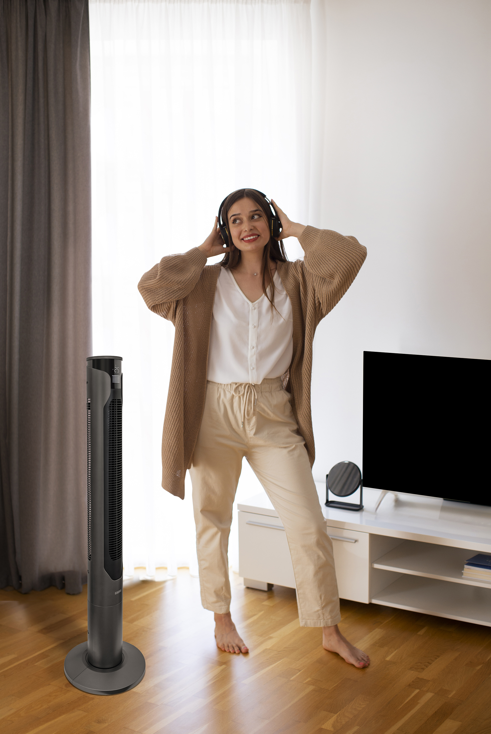 Kobieta w słuchawkach tańczy obok wentylatora i telewizora.